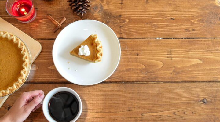 Warm autumn setting with pumpkin pie slice, coffee, and candles on a wooden table.